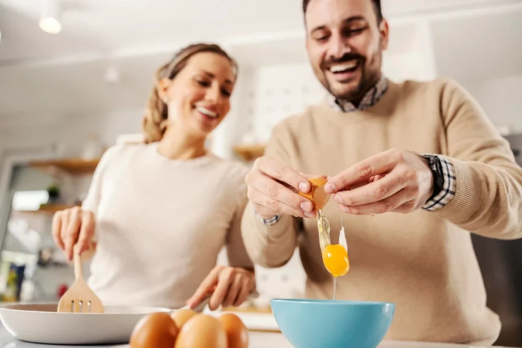Casal sorridente cozinhando juntos na cozinha e quebrando ovos.